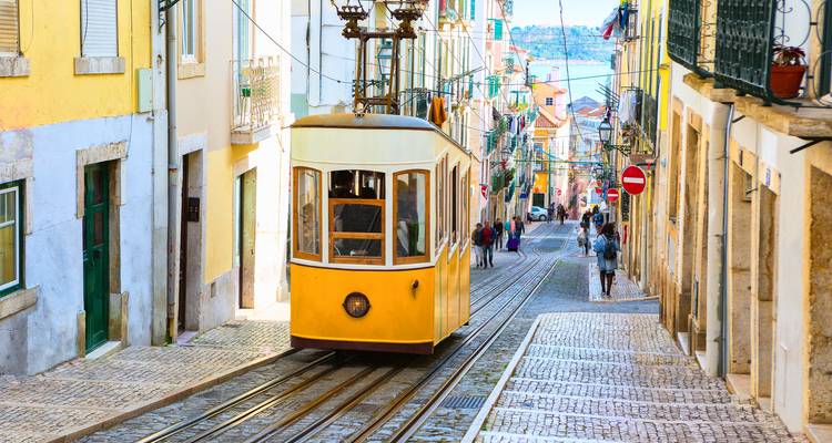Een klassieke gele tram daalt af door een smalle, kleurrijke straat in Lissabon omzoomd door oude gebouwen en voetgangers.
