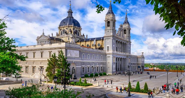 De grootse Almudena Kathedraal en haar plein glinsteren onder een levendige blauwe Madrid hemel.