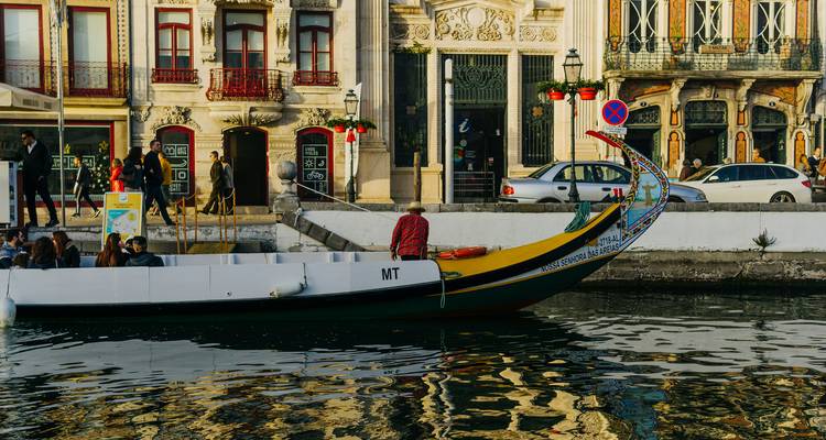 Een beschilderde Moliceiro-boot glijdt langs het kanaal van Aveiro voorbij sierlijke betegelde gevels en wandelende bezoekers.