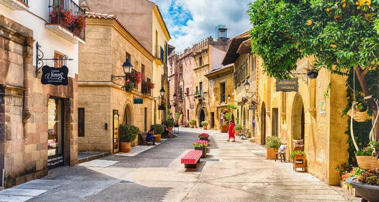 Charmante smalle stenen straat omzoomd met bloemrijke balkons en pastelkleurige gebouwen, een enkele voetganger in het rood wandelend