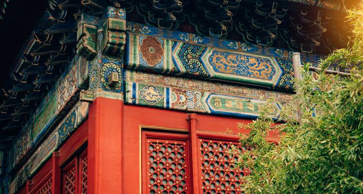 Close-up van rijkelijk beschilderde houten dakranden en rode muren van een traditionele Chinese tempelhoek.