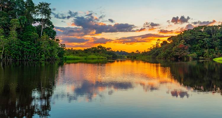 Levendige zonsondergang weerkaatst oranje en paarse tinten over een rustige Amazone-rivier geflankeerd door regenwoud