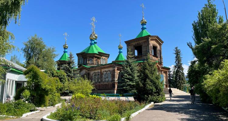 A church with green roofs surrounded by trees against a clear blue sky.