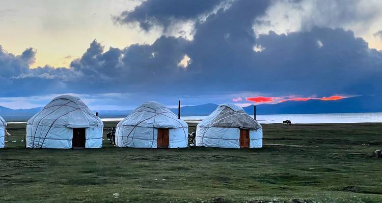 Three yurts on a grassy plain with a dramatic sunset sky.
