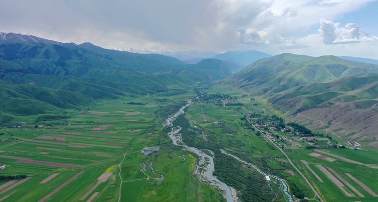 Aerial view of a wide valley with a winding river and surrounding mountains.