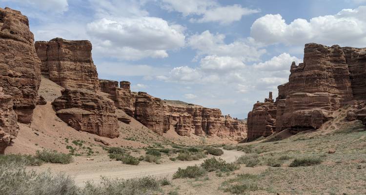 Charyn Canyon with rock formations and a dirt path under a partly cloudy sky.