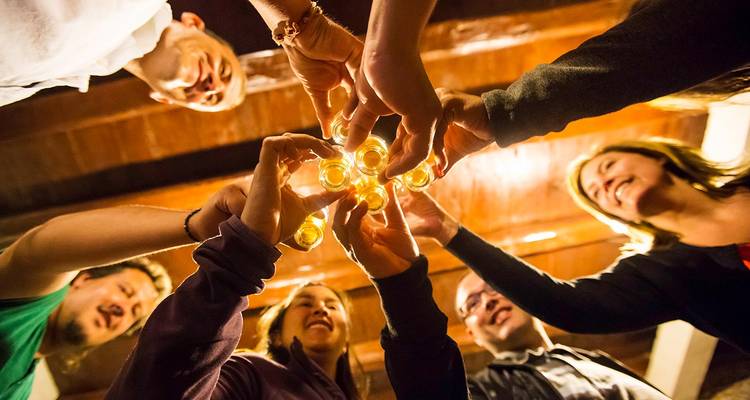 Cercle d'amis levant leurs verres en direction de l'appareil photo sous des poutres en bois chaleureux