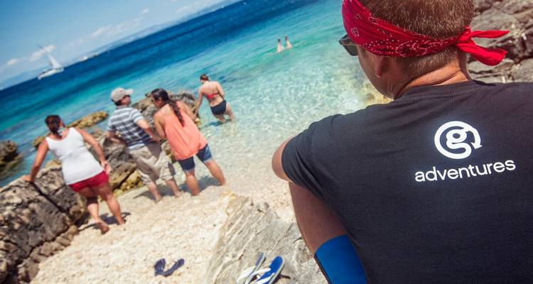 Un petit groupe profitant d'une plage rocheuse aux eaux turquoise cristallines, une personne vêtue d'un t-shirt d'aventure au premier plan
