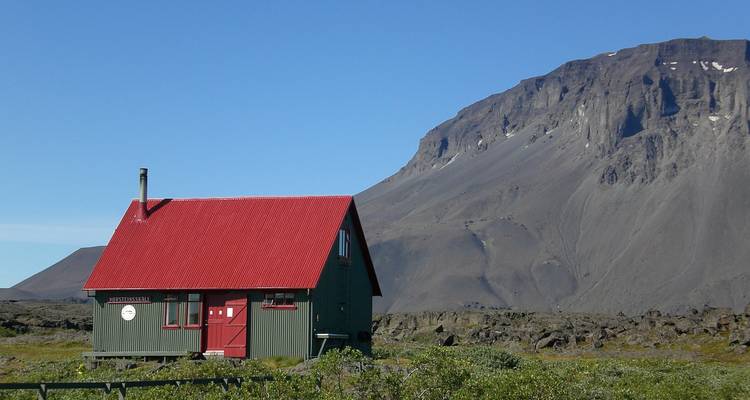 Une petite cabane de montagne avec un toit rouge entourée d'un terrain rocheux.