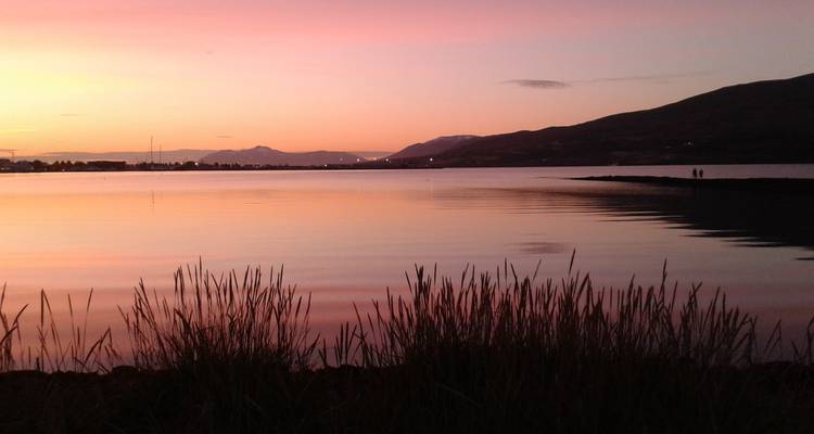Coucher de soleil sur un lac calme avec des montagnes en arrière-plan.