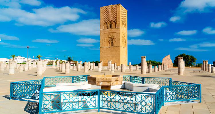 Un site historique avec une haute tour et des colonnes de pierre sous un ciel bleu éclatant.