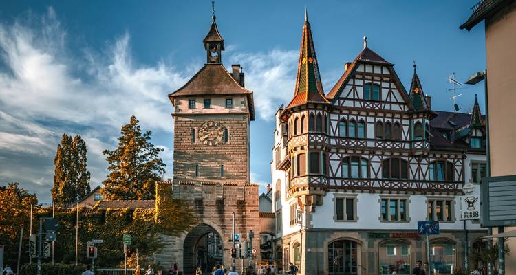 Place de la ville avec des bâtiments historiques et une tour sous un ciel bleu.