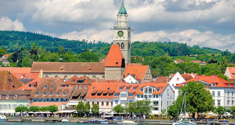 Vue sur le lac d'une ville avec des toits rouges et un clocher d'église proéminent.