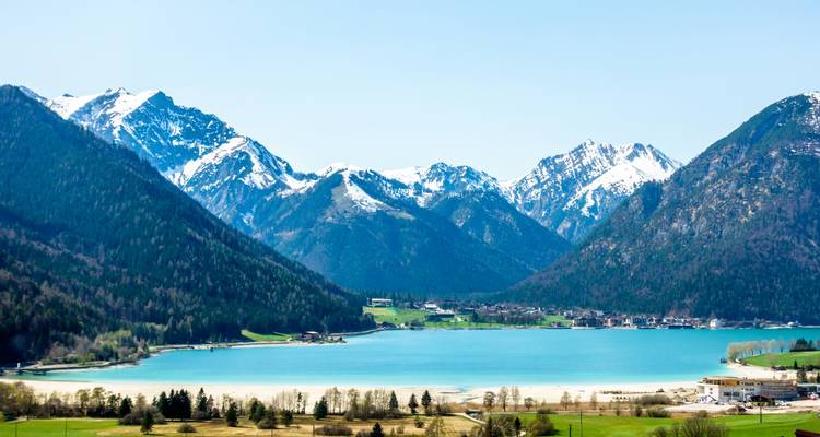 Lac alpin entouré de montagnes enneigées avec un ciel bleu clair.