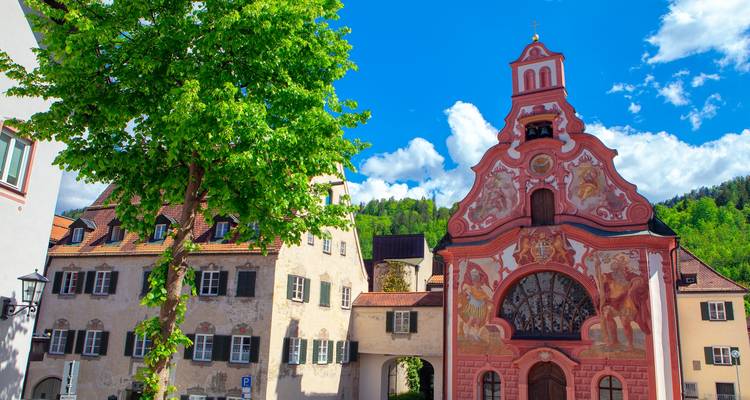 Façade d'église colorée avec un arbre et des bâtiments dans un cadre ensoleillé.