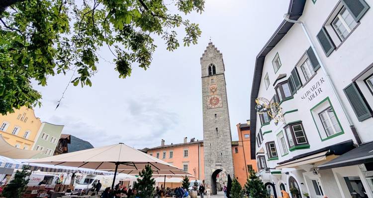 European town square with tall stone tower and market stalls.