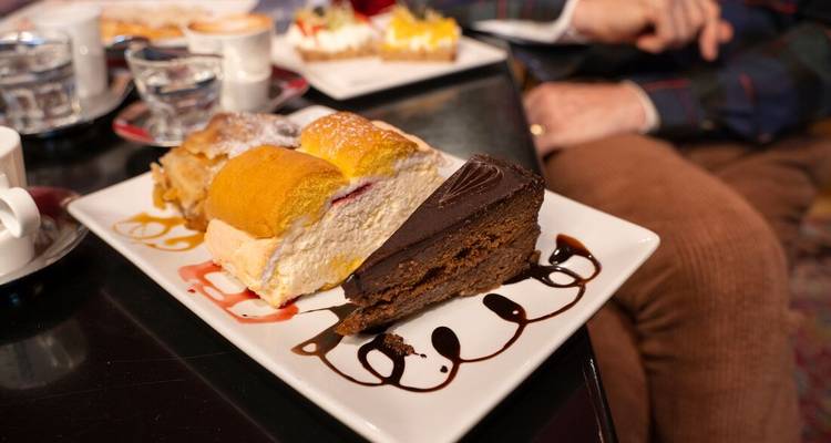 Postres en platos con personas al fondo en lo que parece ser una cafetería.