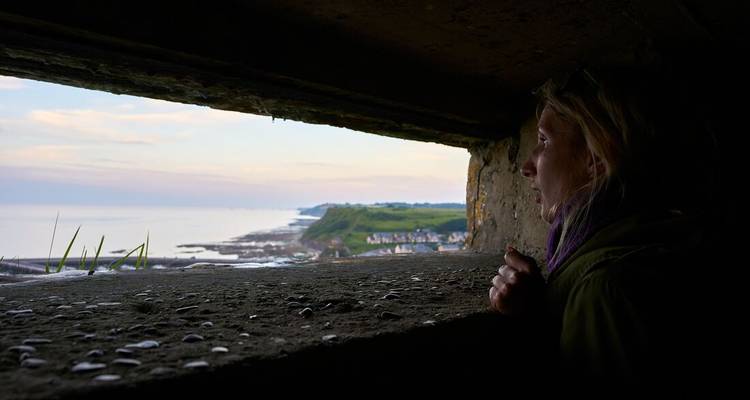 Femme regardant depuis un bunker vers un village côtier