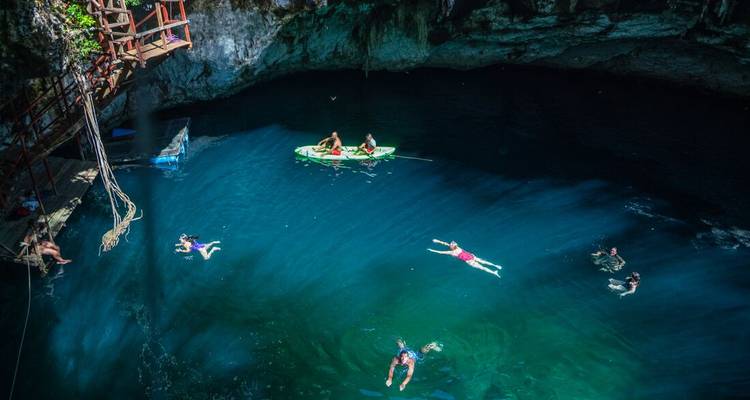 People swimming and kayaking in a clear blue cenote.