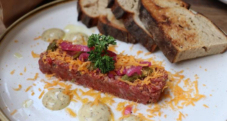 Plat gastronomique avec viande, herbes, sauce et pain.