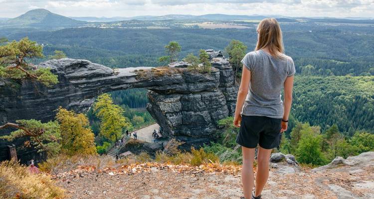Femme contemplant une arche de pierre naturelle dans un paysage forestier.