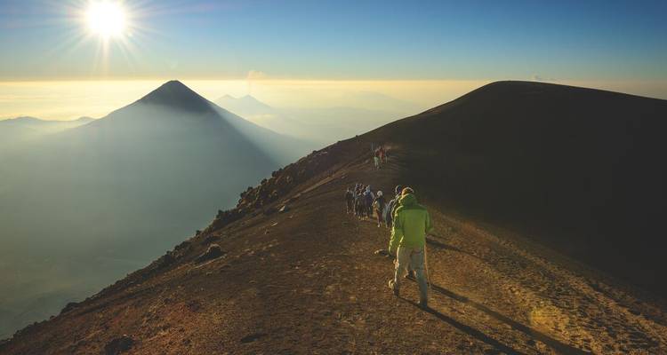 Randonneurs marchant le long d'une crête de montagne avec un volcan au loin au lever du soleil.