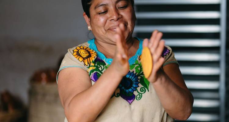 Une femme préparant de la pâte traditionnelle à la main, portant un chemisier brodé coloré.