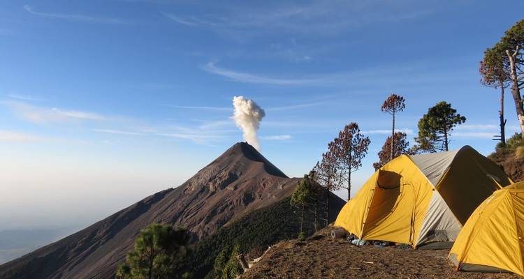 Vue matinale lumineuse d'un camping avec des tentes jaunes près d'un volcan actif.