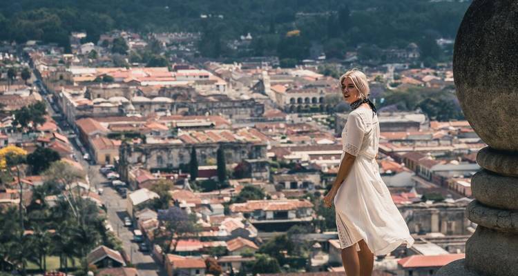 Une femme en robe blanche se tient sur un toit surplombant une ville d'Amérique centrale.