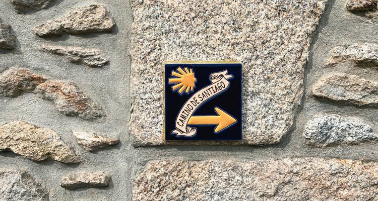 A stone wall with a Camino de Santiago sign indicating direction.