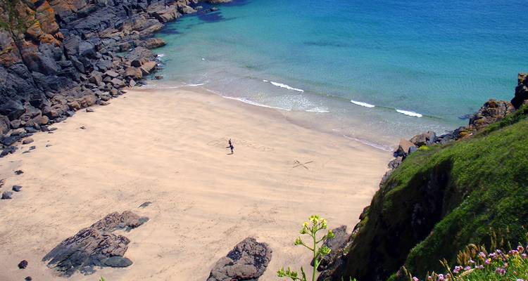 Une plage de sable isolée avec une eau bleue claire vue du sommet d'une falaise.