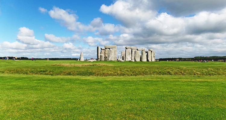 Vue large de Stonehenge au loin avec un ciel bleu dégagé.