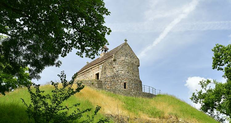 Une ancienne chapelle en pierre sur une colline herbeuse entourée d'arbres.
