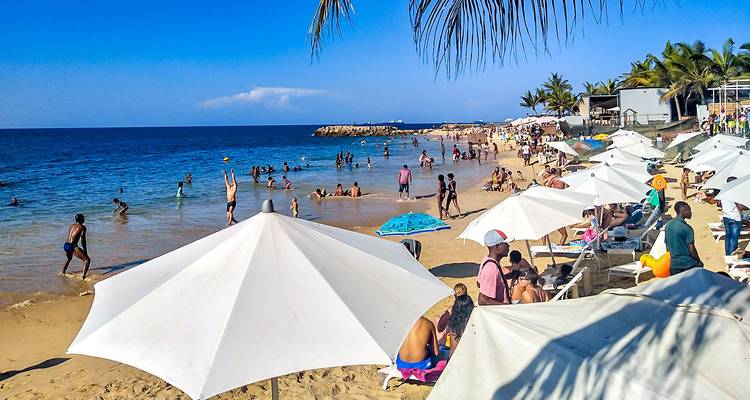 Crowded beach with umbrellas and people swimming.