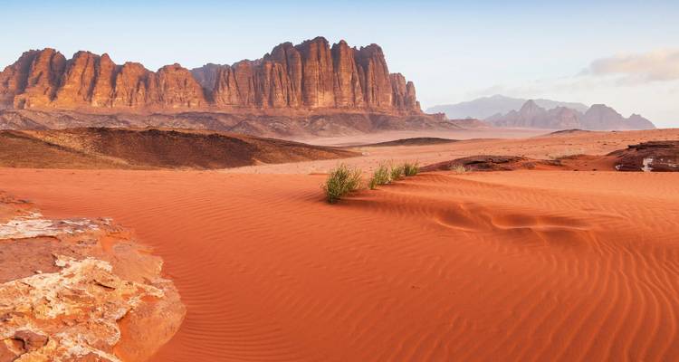 Les dunes de sable rouge ondulées mènent à des montagnes déchiquetées et imposantes dans le vaste désert de Wadi Rum à l'aube.