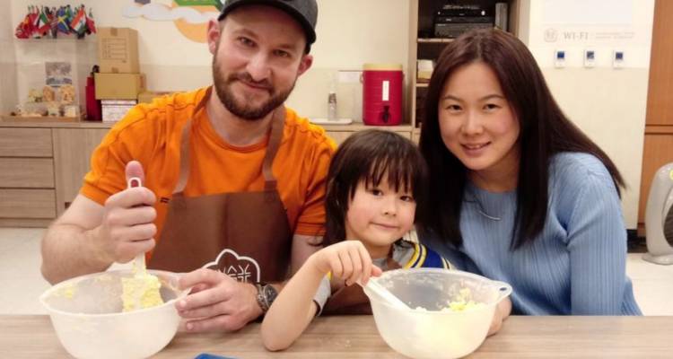 Family smiling while making dough in a kitchen.