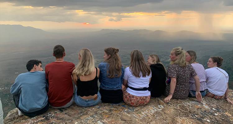 Groep mensen zittend op een rots bij zonsondergang uitkijkend over een vallei.
