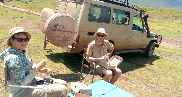 Touristen bei einem Picknick in der Nähe eines Safari-Fahrzeugs.