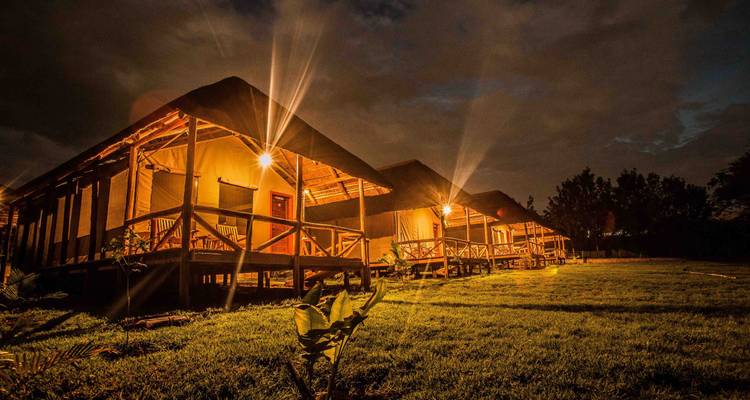 Bungalows de complexe hôtelier illuminés la nuit avec un environnement herbeux.