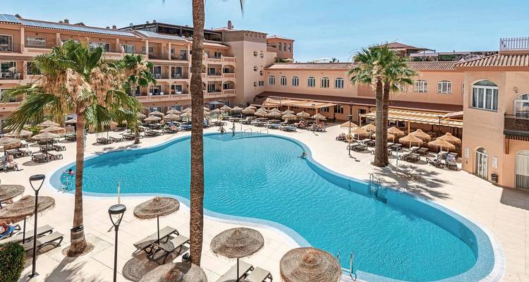 Une zone de piscine d'hôtel avec des palmiers et des chaises longues.