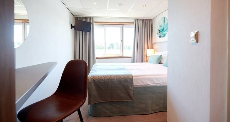 Chambre d'hôtel avec lit, fenêtre et une chaise marron.
