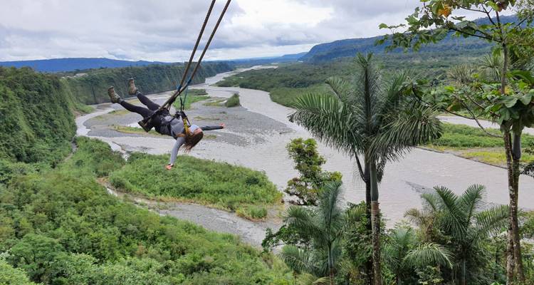 People swinging over a lush valley with a river.