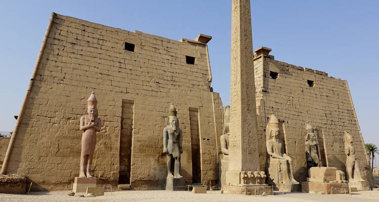 Massive carved stone statues and a towering obelisk at an ancient site.