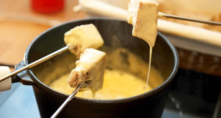 A pot of cheese fondue with skewers of bread.