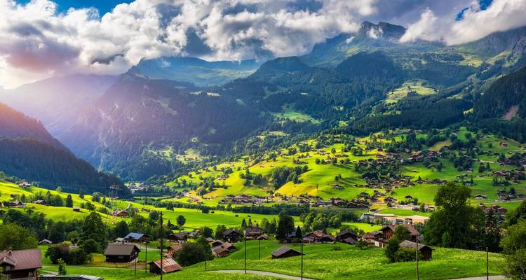 Scenic view of a Swiss village with mountains and scattered clouds.