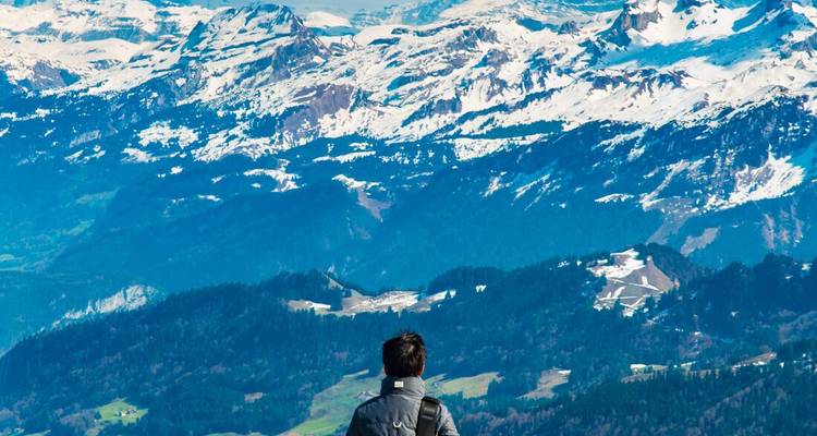 A person looking out at a panoramic mountain range under a clear sky.