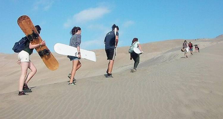 Groupe de personnes escaladant des dunes de sable en portant des planches.