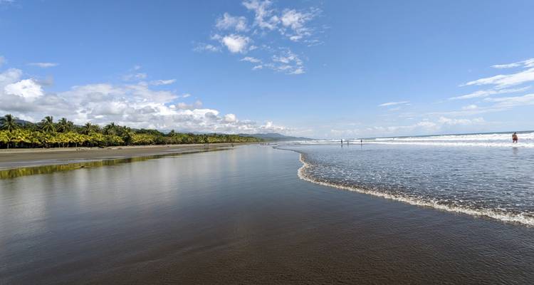 A wide sandy beach with gentle waves under a clear sky.