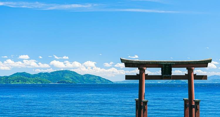 Torii se dressant dans la mer avec des montagnes au loin.