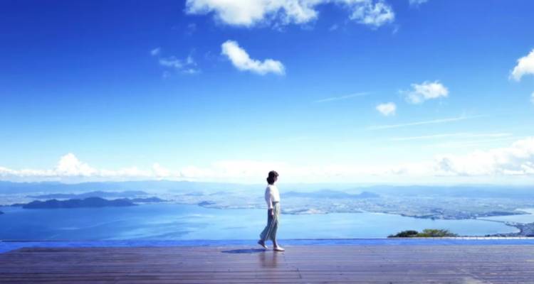 Personne marchant sur une plateforme avec une vue panoramique du lac et des montagnes.